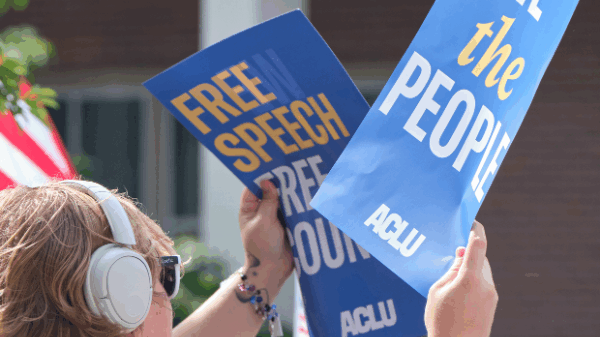A rally attendee holds a sign reading "We the people" and another sign reading "Free speech free country" at the 2025 No Kings protest in Lincoln.