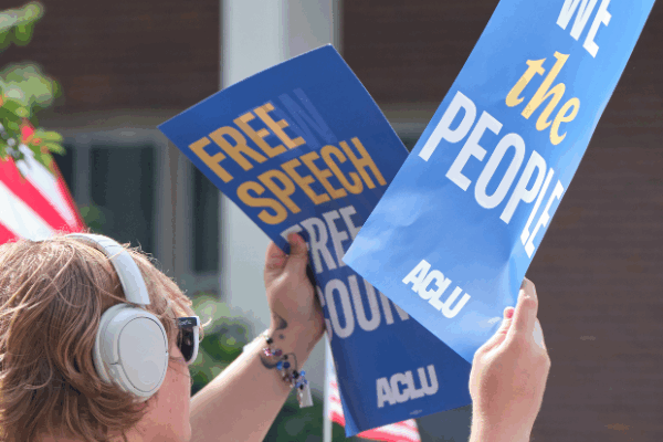 A rally attendee holds a sign reading "We the people" and another sign reading "Free speech free country" at the 2025 No Kings protest in Lincoln.