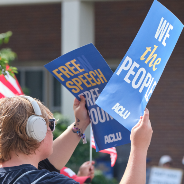 A rally attendee holds a sign reading "We the people" and another sign reading "Free speech free country" at the 2025 No Kings protest in Lincoln.