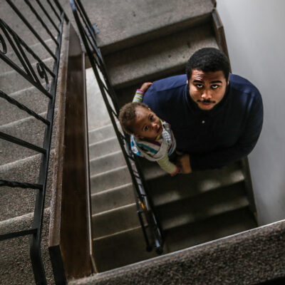Jacob holding his daughter in the stairwell of their apartment building.