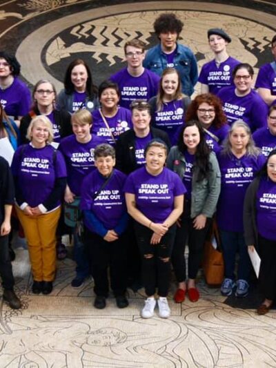 Photo taken from above and angled down. Nebrakans wearing purple shirts pose in the Nebraska Capitol Rotunda