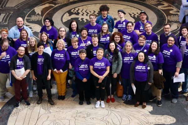 Photo taken from above and angled down. Nebrakans wearing purple shirts pose in the Nebraska Capitol Rotunda