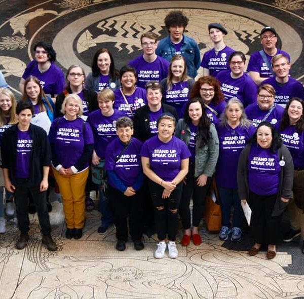 Photo taken from above and angled down. Nebrakans wearing purple shirts pose in the Nebraska Capitol Rotunda