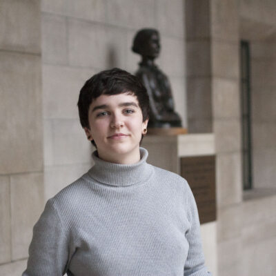 Mar Lee wears a light grey turtleneck, standing in front of a bust