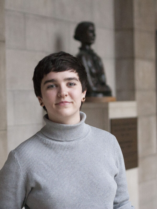 Mar Lee wears a light grey turtleneck, standing in front of a bust