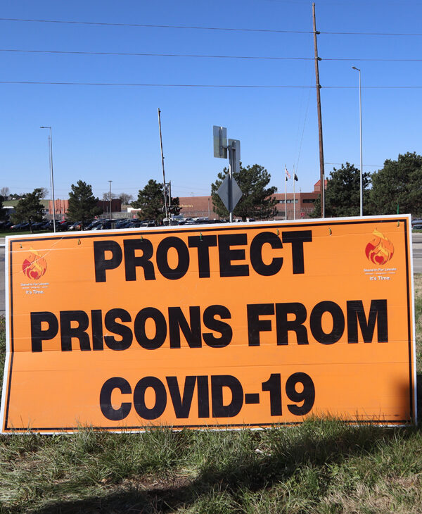 Rex Walton and Paul Feilmann hold a sign reading "Protect prisons from COVID-19" outside of the Nebraska State Penitentiary.