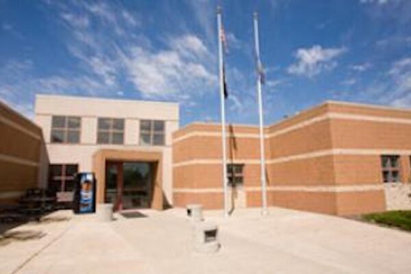 a photo of the Nebraska Correctional Youth Facilities building in Omaha; the building is very square with yellow/orange walls with three white/cream stripes across them. The entrance of the building is the same color as the stripes, outlined in the orange