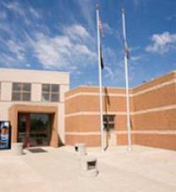 a photo of the Nebraska Correctional Youth Facilities building in Omaha; the building is very square with yellow/orange walls with three white/cream stripes across them. The entrance of the building is the same color as the stripes, outlined in the orange