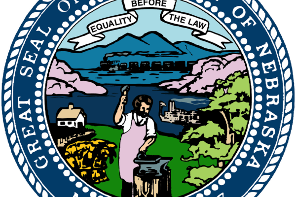 A landscape featuring Sandhills, a train, the Missouri River, a tree, wheat, a house, a steamboat, and blacksmith. A banner in the sky says "Equality Before the Law". A blue circle border, in white "Great Seal of the State of Nebraska March 1st 1867"