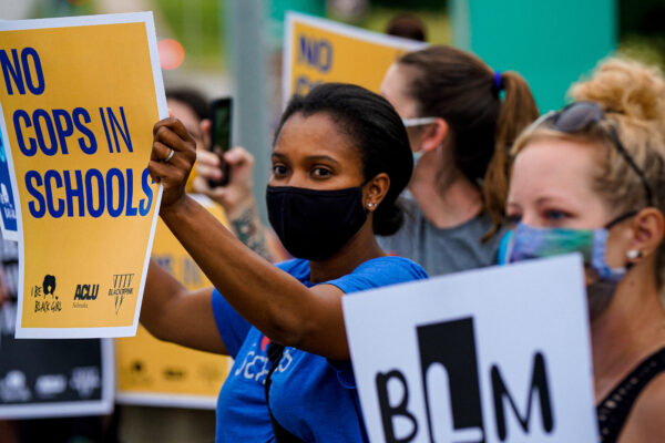 A protester holds a sign reading "No Cops in Schools."