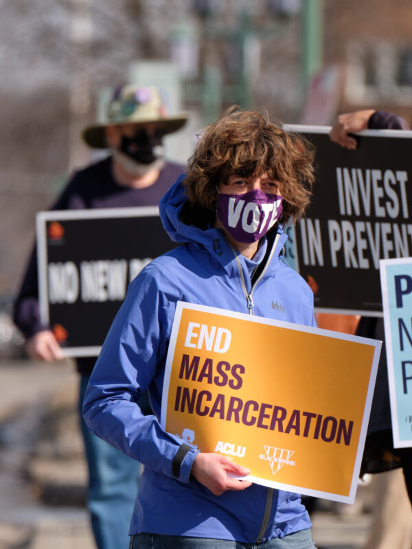 Protesters stand alongside a Lincoln street, holding signs that read "End mass incarceration" and "People not prisons."