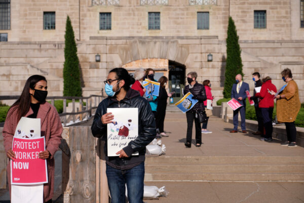 Community members stand at the east entrance of the Nebraska State Capitol, holding signs encouraging protections for essential workers.