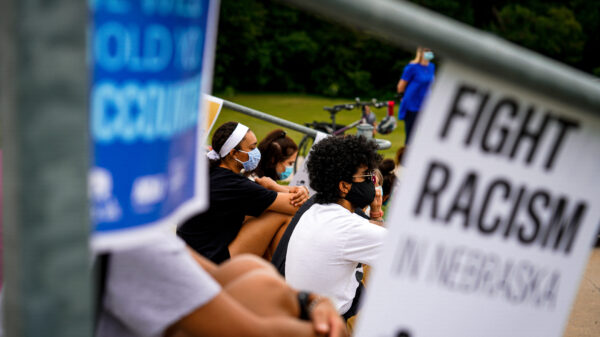 Students sit listening to a speaker at an Educators for Black Lives rally. A sign nearby reads Fight Racism in Nebraska.
