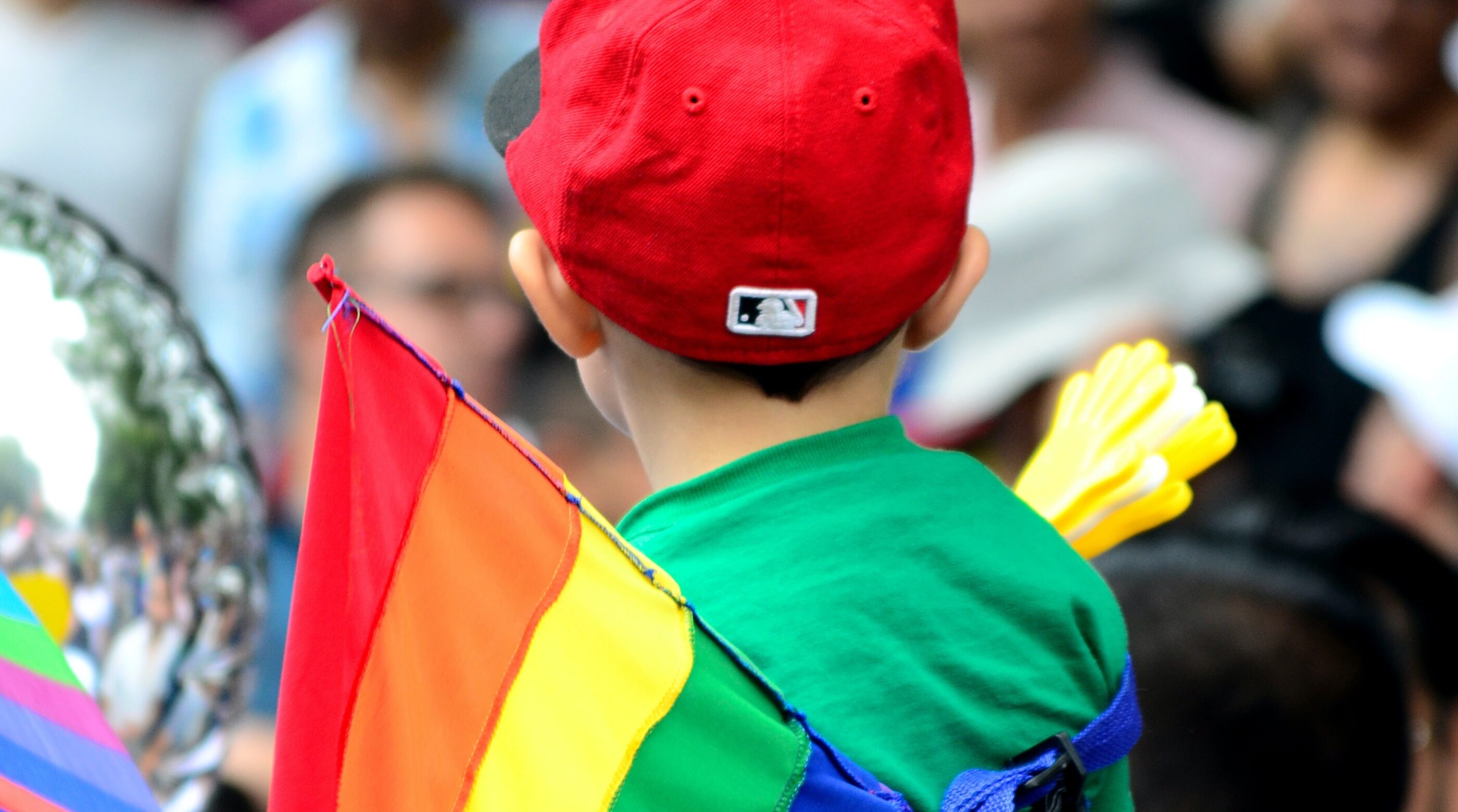 A child stands near a Pride flag.