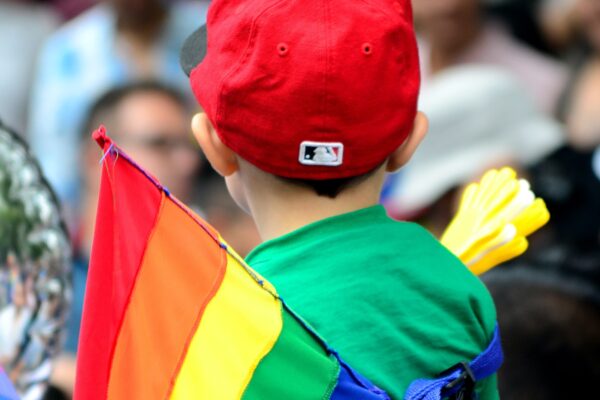 A child stands near a Pride flag.