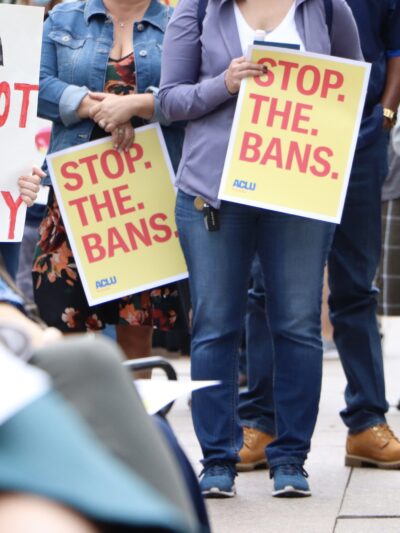 Attendees hold signs at an Omaha reproductive rights rally, reading "Stop. The. Bans."