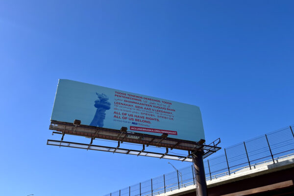 A light blue billboard shows the Statue of Liberty's torch next to translated text, all reading "All of us have rights. All of us belong."