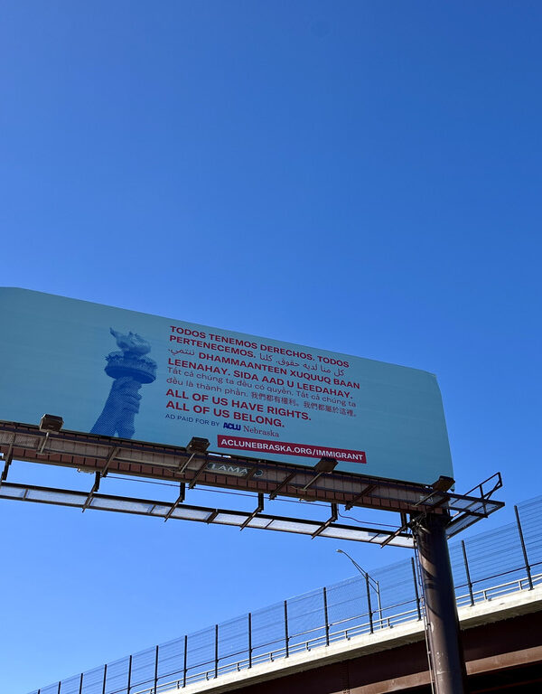 A light blue billboard shows the Statue of Liberty's torch next to translated text, all reading "All of us have rights. All of us belong."