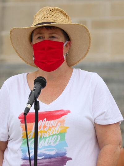 Abbi speaks at a rally outside the Nebraska State Capitol wearing a rainbow shirt that says All You Need is Love.