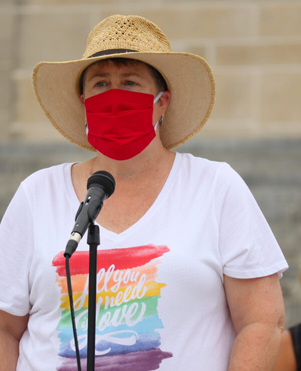 Abbi speaks at a rally outside the Nebraska State Capitol wearing a rainbow shirt that says All You Need is Love.