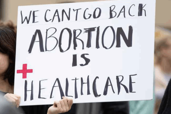 A person at a rally holds a handmade sign that says, "We can't go back. Abortion is Healthcare."