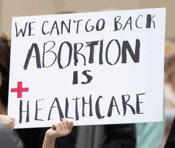 A person at a rally holds a handmade sign that says, "We can't go back. Abortion is Healthcare."