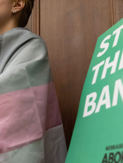 A Nebraskan wrapped in the trans flag listens to testimony during a committee hearing for the near-total abortion ban.