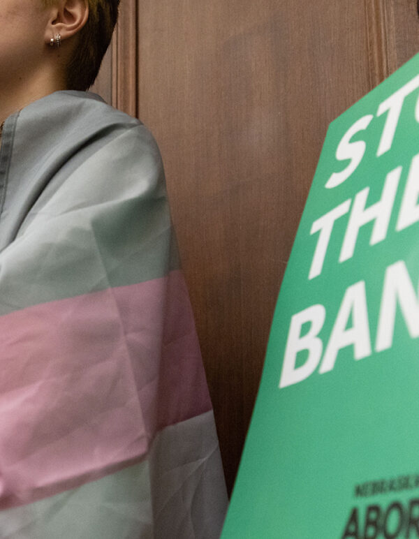 A Nebraskan wrapped in the trans flag listens to testimony during a committee hearing for the near-total abortion ban.