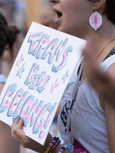A rally attendee holds a sign reading trans kids belong.