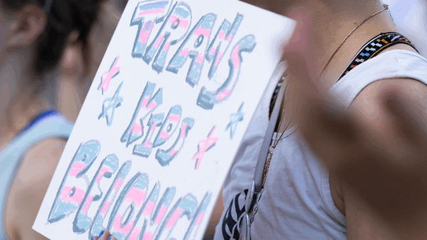 A rally attendee holds a sign reading trans kids belong.