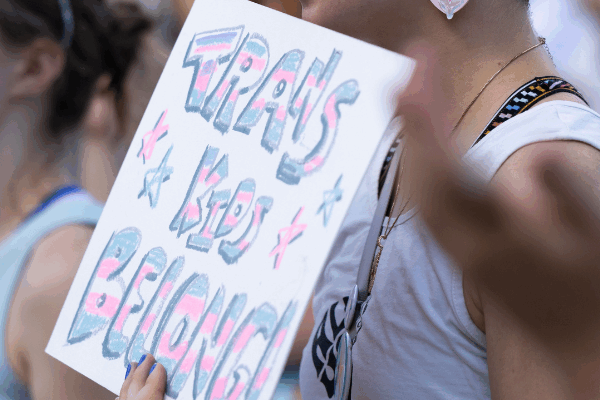 A rally attendee holds a sign reading trans kids belong.