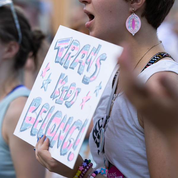 A rally attendee holds a sign reading trans kids belong.