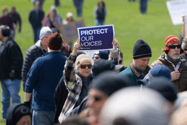 A rally attendee holds up a sign reading "protect our voices"