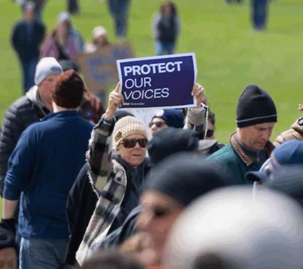 A rally attendee holds up a sign reading "protect our voices"