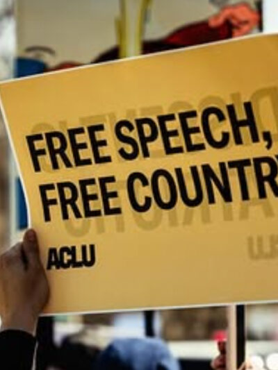 A rally attendee in Omaha holds an ACLU sign reading "FREE SPEECH, FREE COUNTRY."