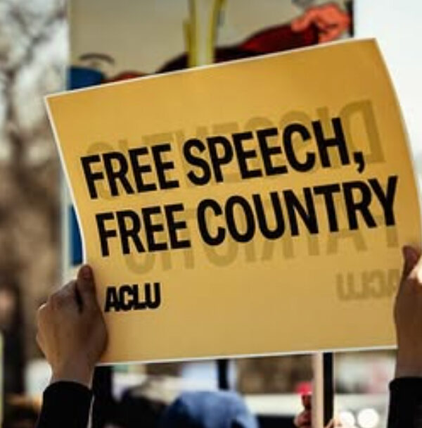 A rally attendee in Omaha holds an ACLU sign reading "FREE SPEECH, FREE COUNTRY."