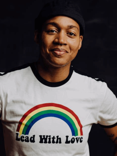 A photograph of a smiling Black person in a white shirt reading "Lead with Love." Over the words is a rainbow.