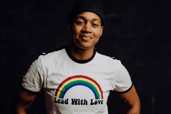 A photograph of a smiling Black person in a white shirt reading "Lead with Love." Over the words is a rainbow.