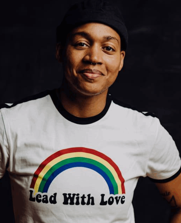 A photograph of a smiling Black person in a white shirt reading "Lead with Love." Over the words is a rainbow.
