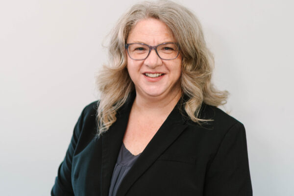 Jennifer Houlden, a white woman in glasses with long hair and a black blazer, poses for a photo.