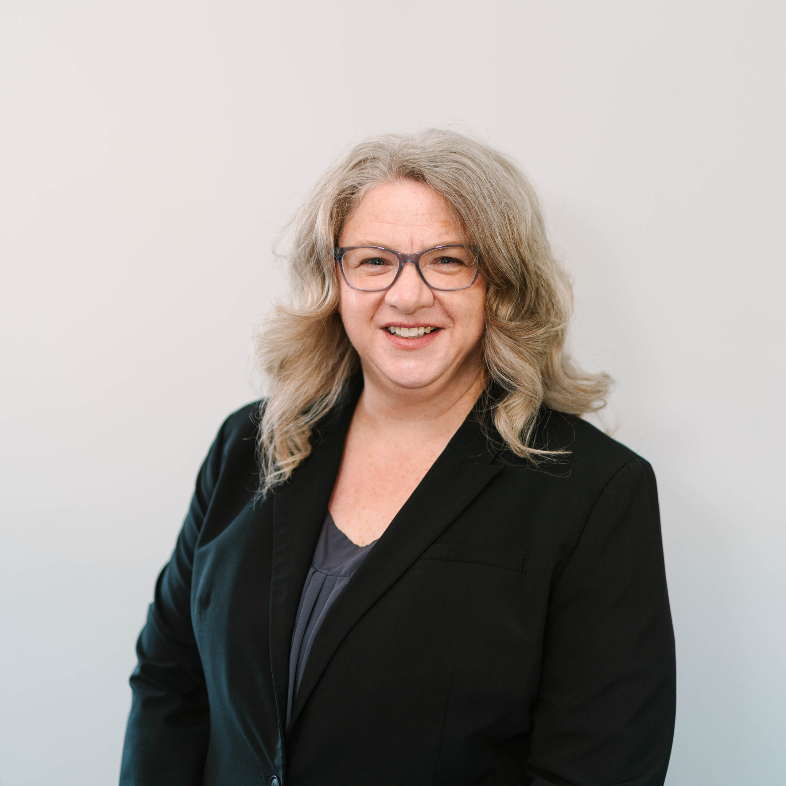 Jennifer Houlden, a white woman in glasses with long hair and a black blazer, poses for a photo.