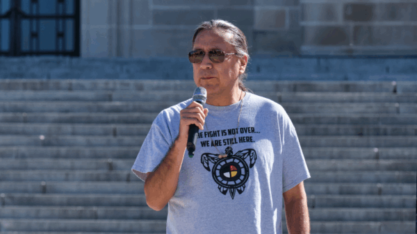 Kevin Abourezk speaks in front of the Nebraska State Capitol wearing a shirt that reads "The fight is not over. We are still here."