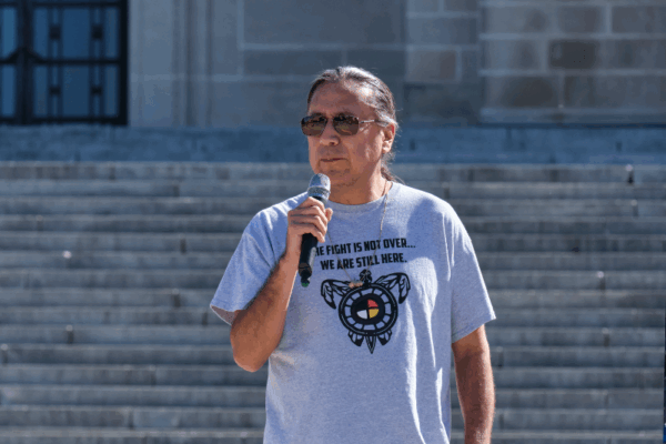 Kevin Abourezk speaks in front of the Nebraska State Capitol wearing a shirt that reads "The fight is not over. We are still here."
