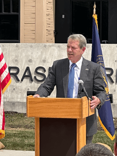 Gov. Jim Pillen stands at a podium in front of a Nebraska Army National Guard facility.