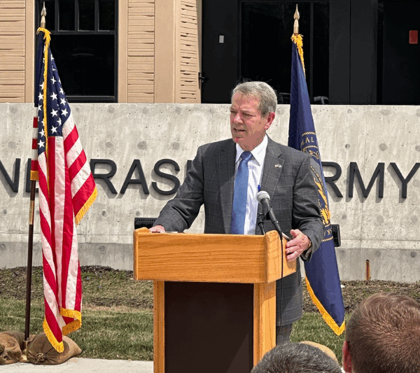 Gov. Jim Pillen stands at a podium in front of a Nebraska Army National Guard facility.