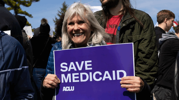 A rally attendee in Omaha holds a purple and white sign reading Save Medicaid.
