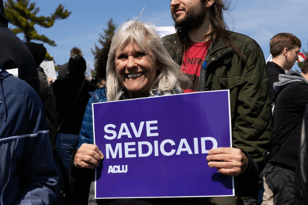 A rally attendee in Omaha holds a purple and white sign reading Save Medicaid.