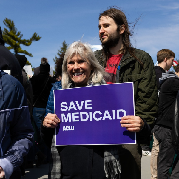 A rally attendee in Omaha holds a purple and white sign reading Save Medicaid.