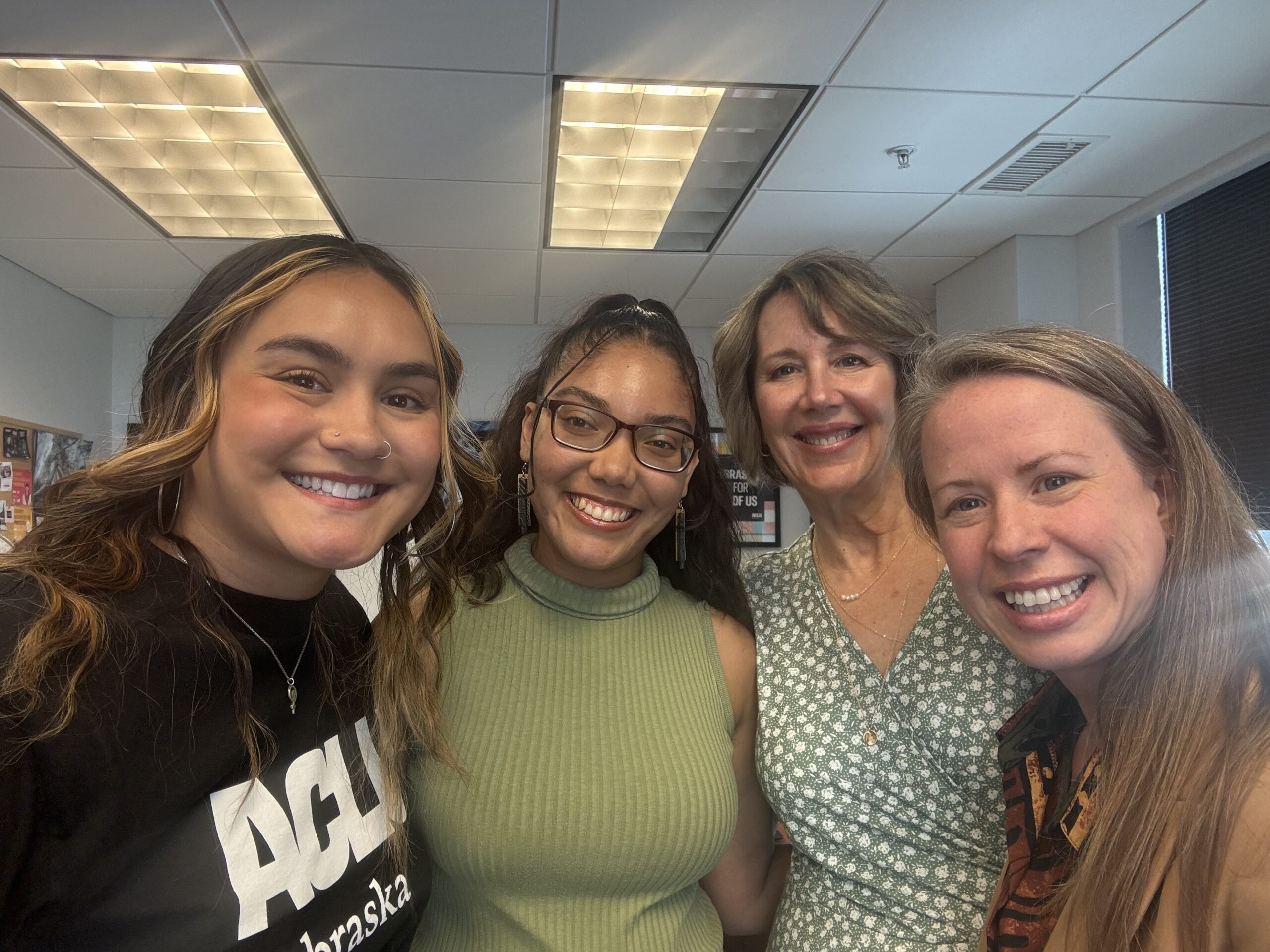 Four women smile at the camera in a group image inside the ACLU of Nebraska office.