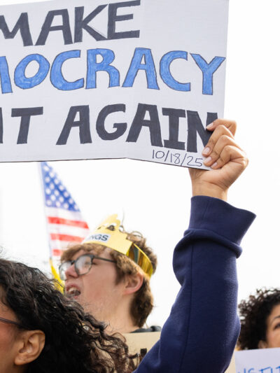 Omahans gather for a protest against federal overreach. A protester in the foreground holds a sign reading "Make Democracy Great again."
